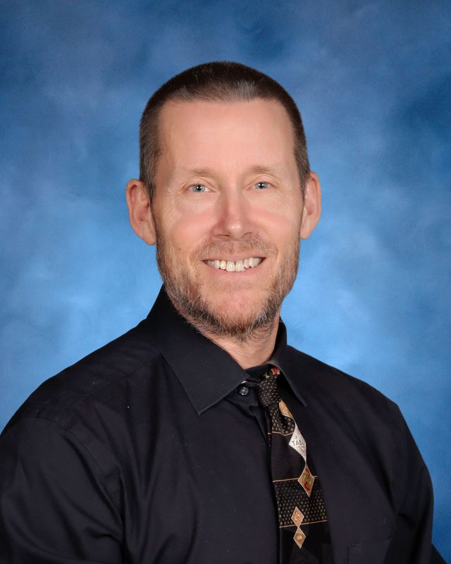 A man with short hair and a trimmed beard smiles, wearing a black shirt and tie—captured at St. Paul's School, a top Northshore private school.