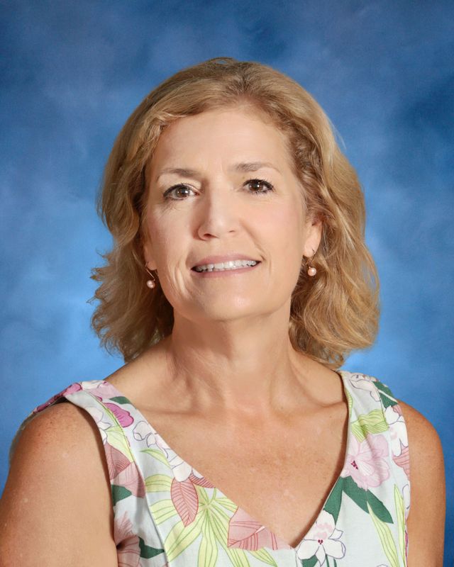 A woman with shoulder-length blonde hair smiles in front of a blue background, representing St. Paul's School on the Northshore.