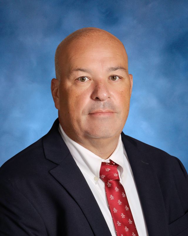 A man in a suit and red patterned tie poses for a formal portrait, representing St. Paul’s School, a leading private school on the Northshore.