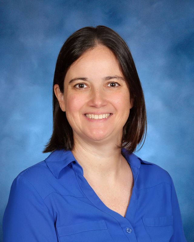 A woman with straight dark hair, wearing a blue collared shirt, smiles at the camera—representing St. Paul's School on the Northshore.