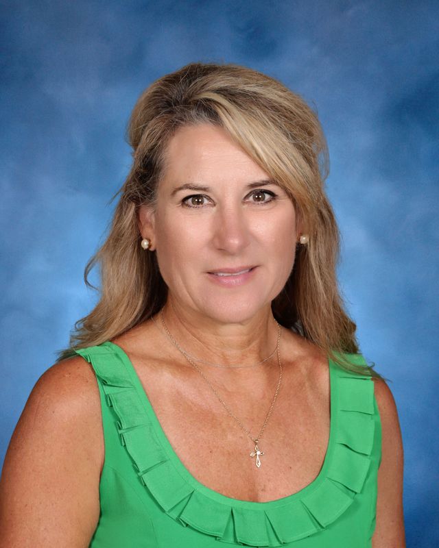 A woman with long blonde hair in a green sleeveless top poses before a blue backdrop at St. Paul's School on the Northshore.