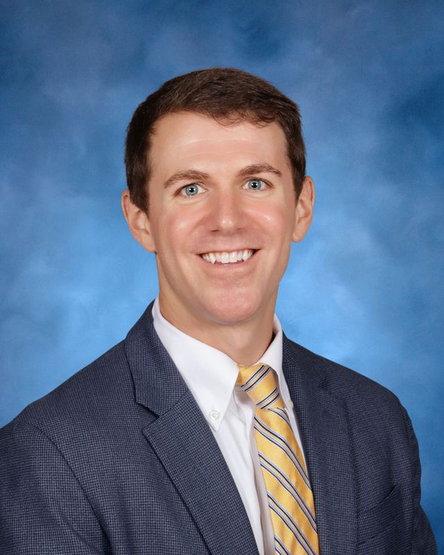 A man in a suit and yellow striped tie smiles, representing St. Paul's School, a leading private school on the Northshore.