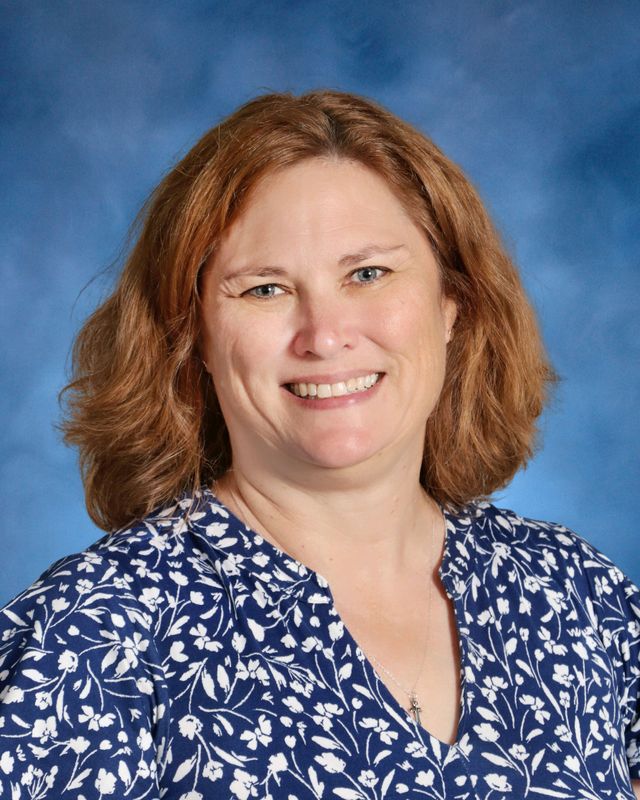 A woman with shoulder-length brown hair smiles at the camera, wearing a blue and white floral blouse at St. Paul’s School.