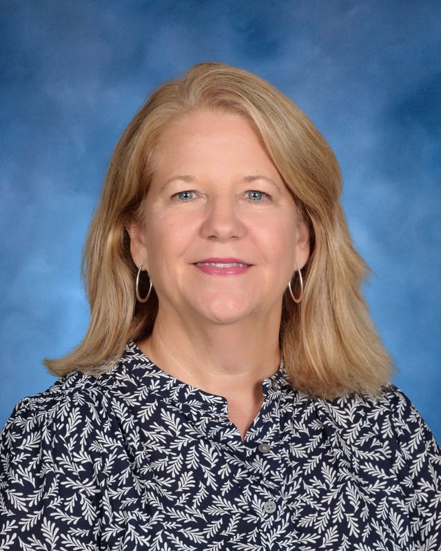 Woman with shoulder-length blonde hair in a patterned blouse, representing St. Paul's School, in front of a blue studio background.