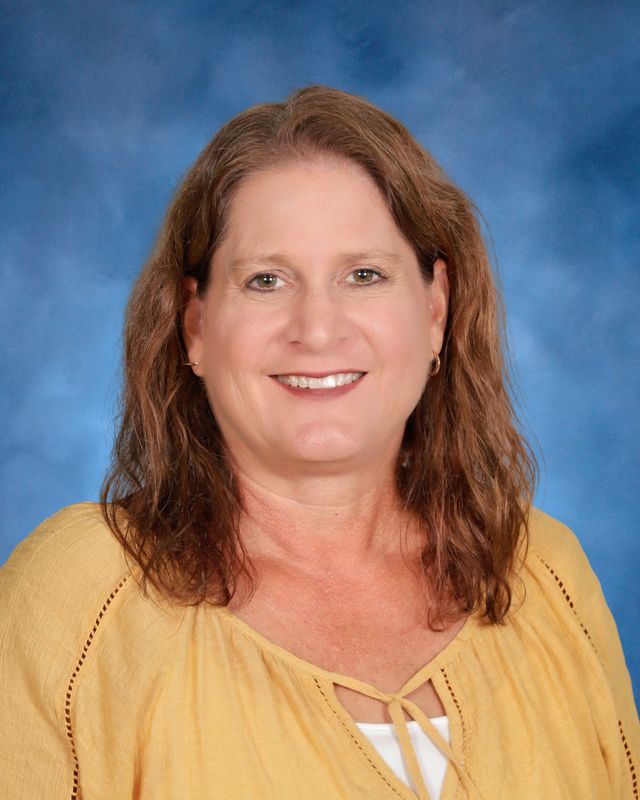 A woman with shoulder-length brown hair, wearing a yellow top, smiles at the camera in front of St. Paul's School's blue background.