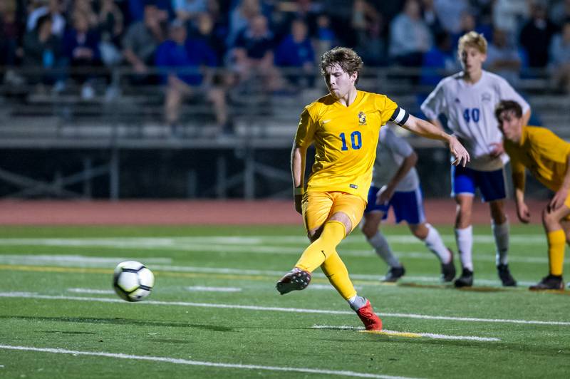 A soccer player in a yellow St. Paul's School uniform prepares to kick a ball, with teammates and opponents visible in the background.