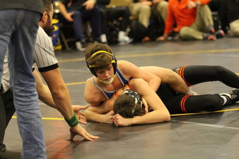 Two young wrestlers from St. Paul's School compete as a referee watches, with spectators from private schools on the Northshore in the background.