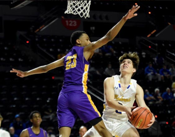 A St. Paul's School player in white drives to the basket as a defender in purple tries to block him.