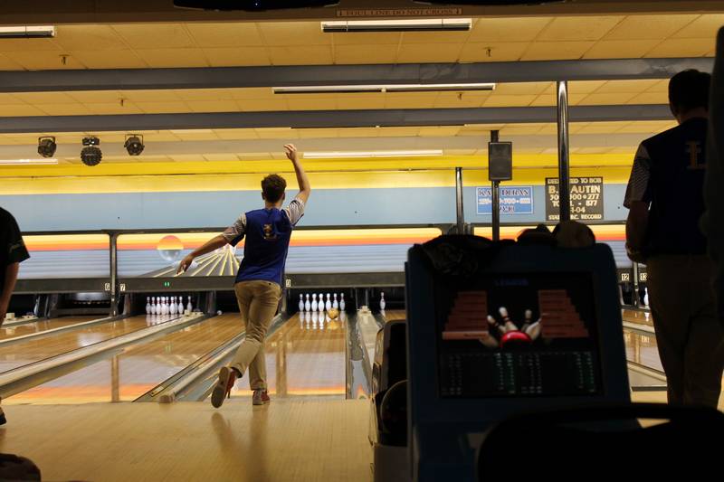 A person at a bowling alley releases a ball down the lane; a St. Paul's School scoring monitor is visible in the foreground.