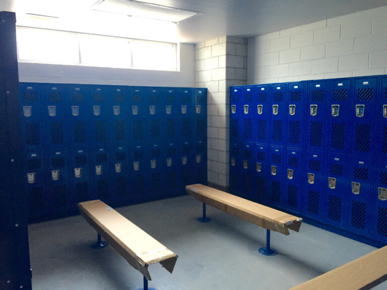 A locker room at St. Paul's School with blue metal lockers, wooden benches, and sunlight streaming through a high window.