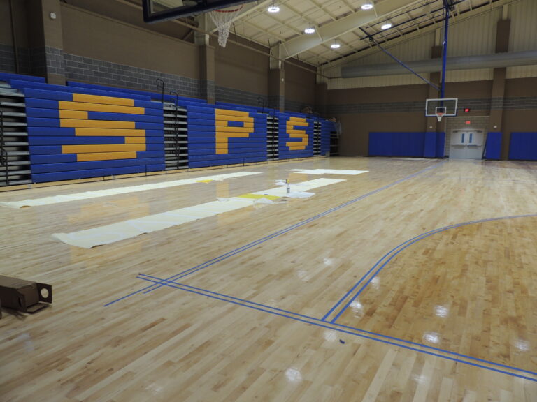 A gymnasium at St. Paul's School with wooden floors, blue and yellow bleachers, and lined tape marking court areas.