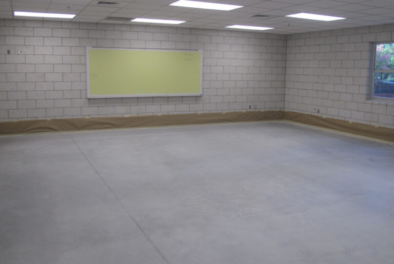 An empty classroom at St. Paul's School features a concrete floor, cinder block walls, a large window, and a whiteboard on one wall.
