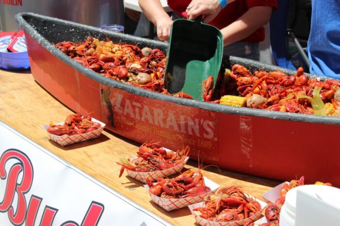 At a St. Paul's School event, a person serves crawfish and vegetables from a boat-shaped container into trays outdoors.