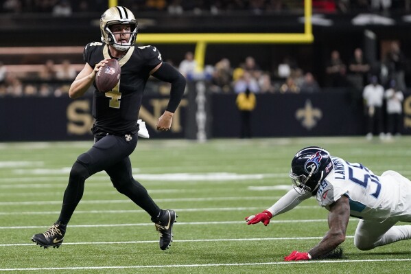 A New Orleans Saints quarterback runs with the football as a Titans defender attempts to tackle him during the 2024 season.