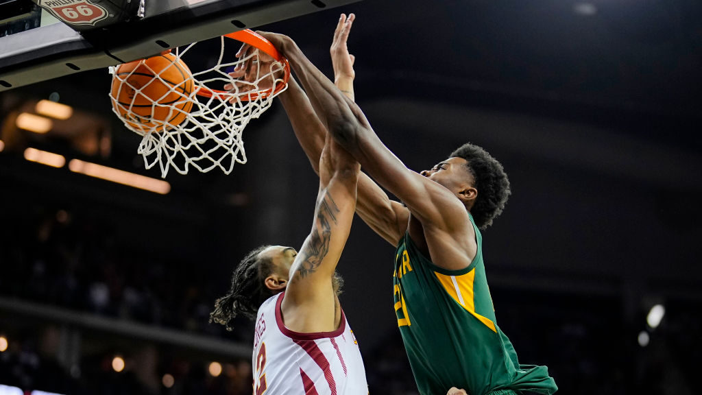A basketball player in a green and yellow uniform blocks a dunk by Zion Williamson during the Pelicans 2024-25 season.