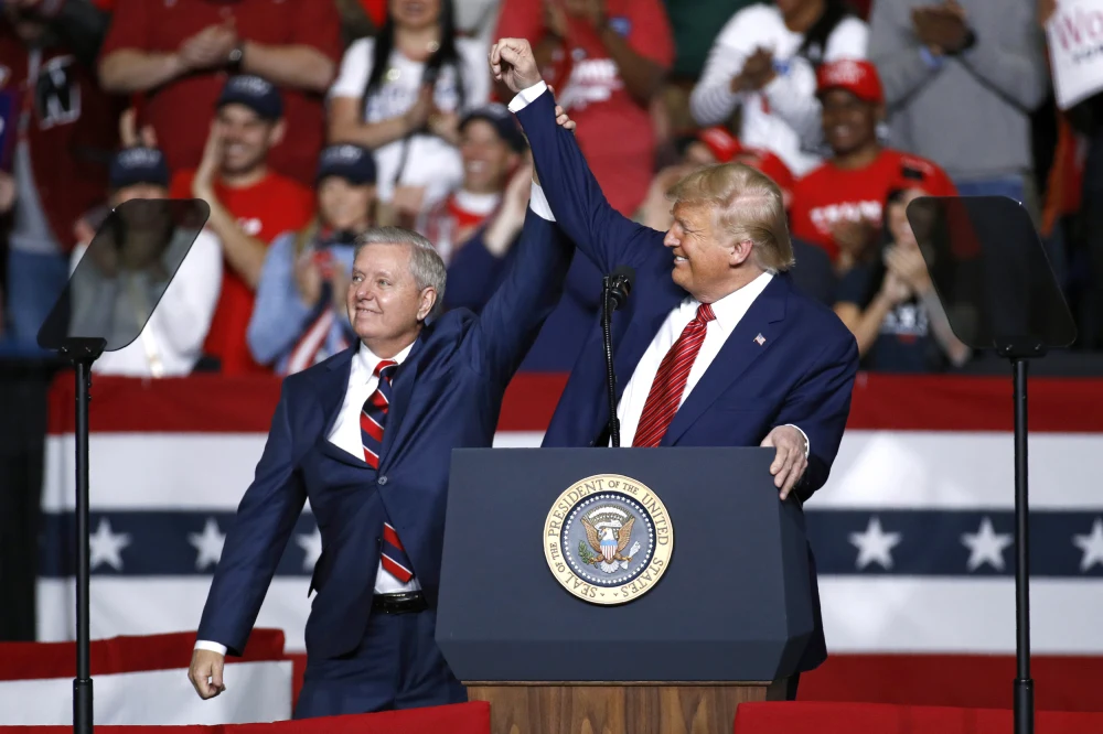 Former President Donald Trump raises a man’s hand on stage at a rally amid cheers and U.S. flag bunting, energizing the 2024 presidential election crowd.